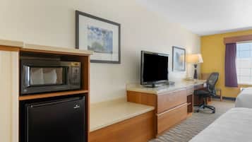 A hotel room with a bed, a desk with a computer, a microwave, and a refrigerator.