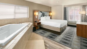Une chambre d’hôtel moderne avec un grand lit, une salle de bain séparée avec une baignoire et une fenêtre avec des rideaux.