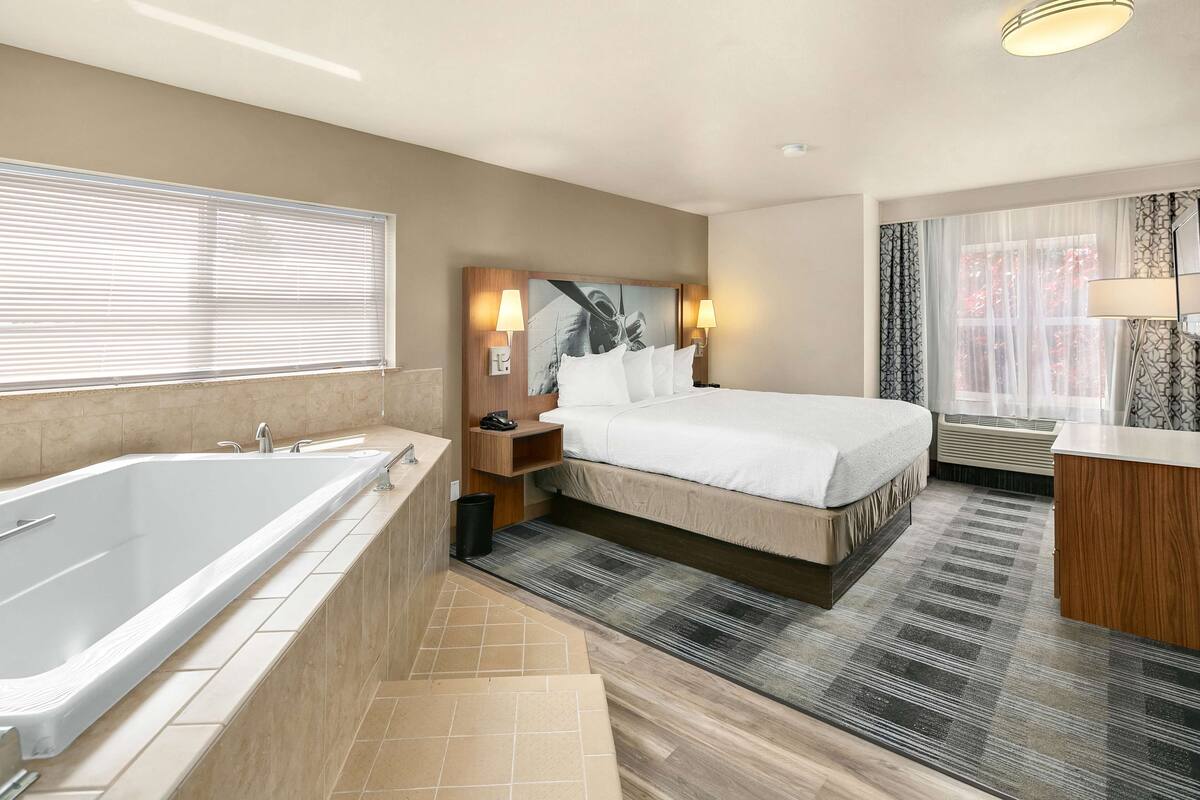 Une chambre d’hôtel moderne avec un grand lit, une salle de bain séparée avec une baignoire et une fenêtre avec des rideaux.