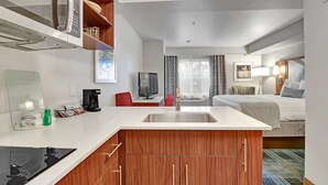 Une chambre d’hôtel de taille réduite, équipée d’une kitchenette, d’un lit, d’une télévision et d’une salle de bain.