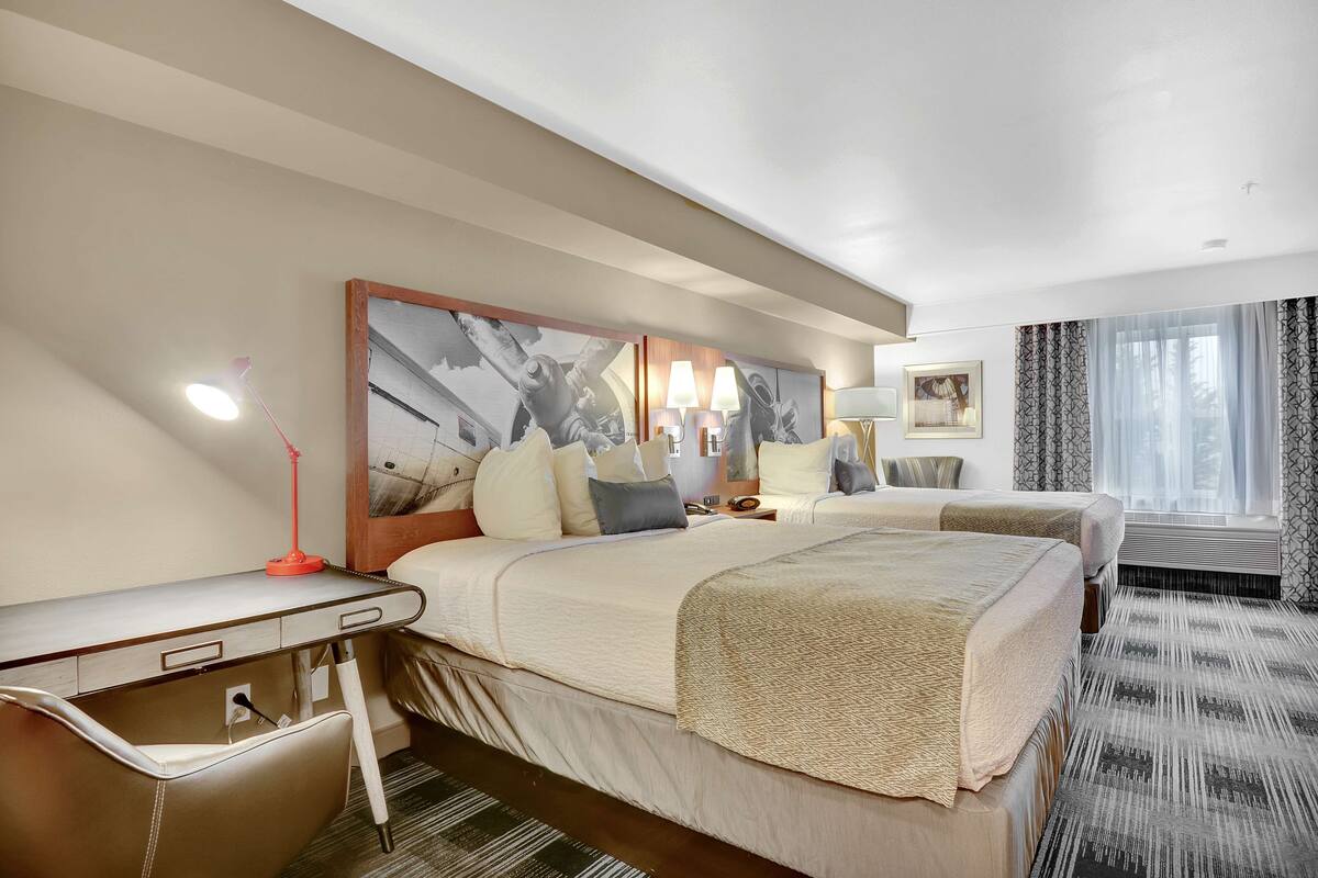 Une chambre d’hôtel avec deux lits, un bureau, une chaise, une lampe et un grand tableau encadré au mur.