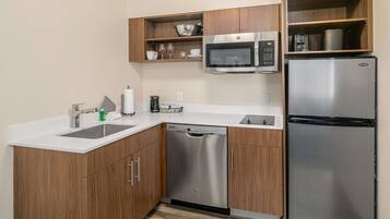 A compact kitchen with wooden cabinets, a stainless steel dishwasher, a microwave, and a refrigerator.