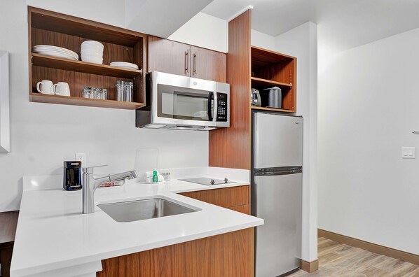 A modern kitchen with white countertops, stainless steel appliances, wooden cabinetry, and a built-in microwave.