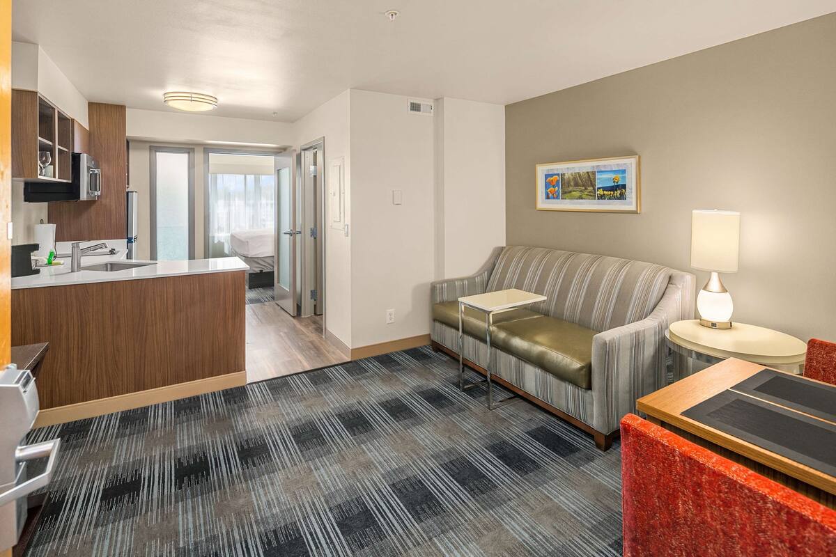 Une chambre d’hôtel moderne équipée d’une kitchenette, d’un canapé, d’une petite table et d’une lampe.