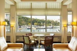 Habitación de hotel con un ventanal grande, una mesa redonda, cuatro sillas y dos lámparas.