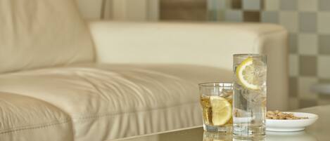 A glass of water with a lemon slice on a table in a room with a beige sofa and a checkered wall.