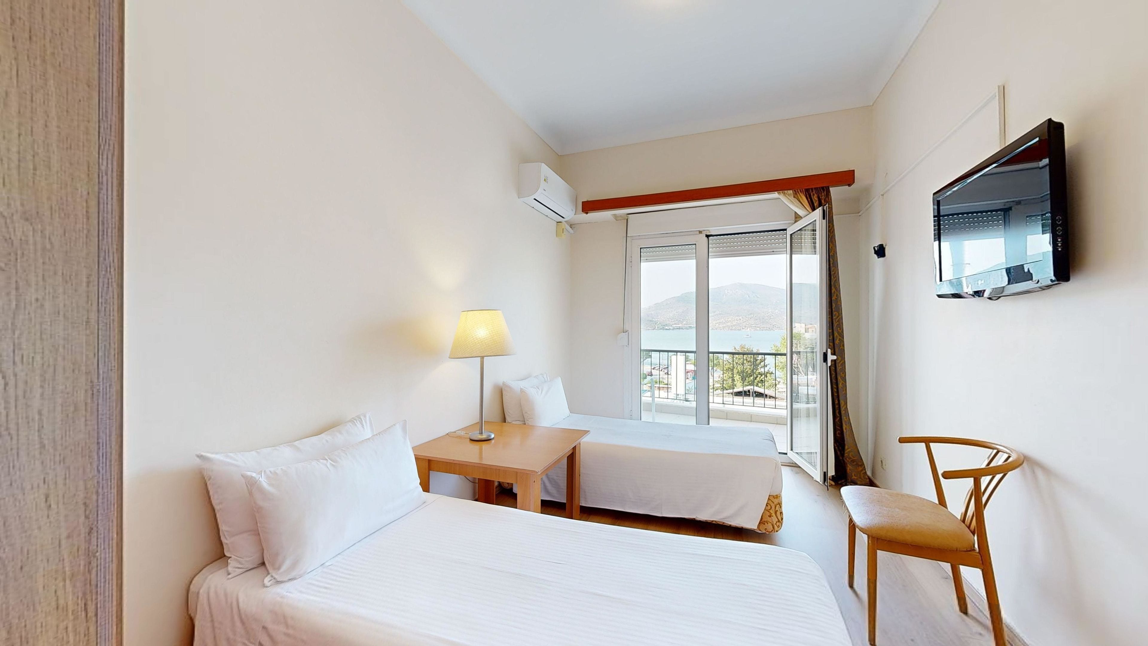 Una camera d'albergo con due letti, una scrivania, una sedia, una televisione e un balcone con vista.
