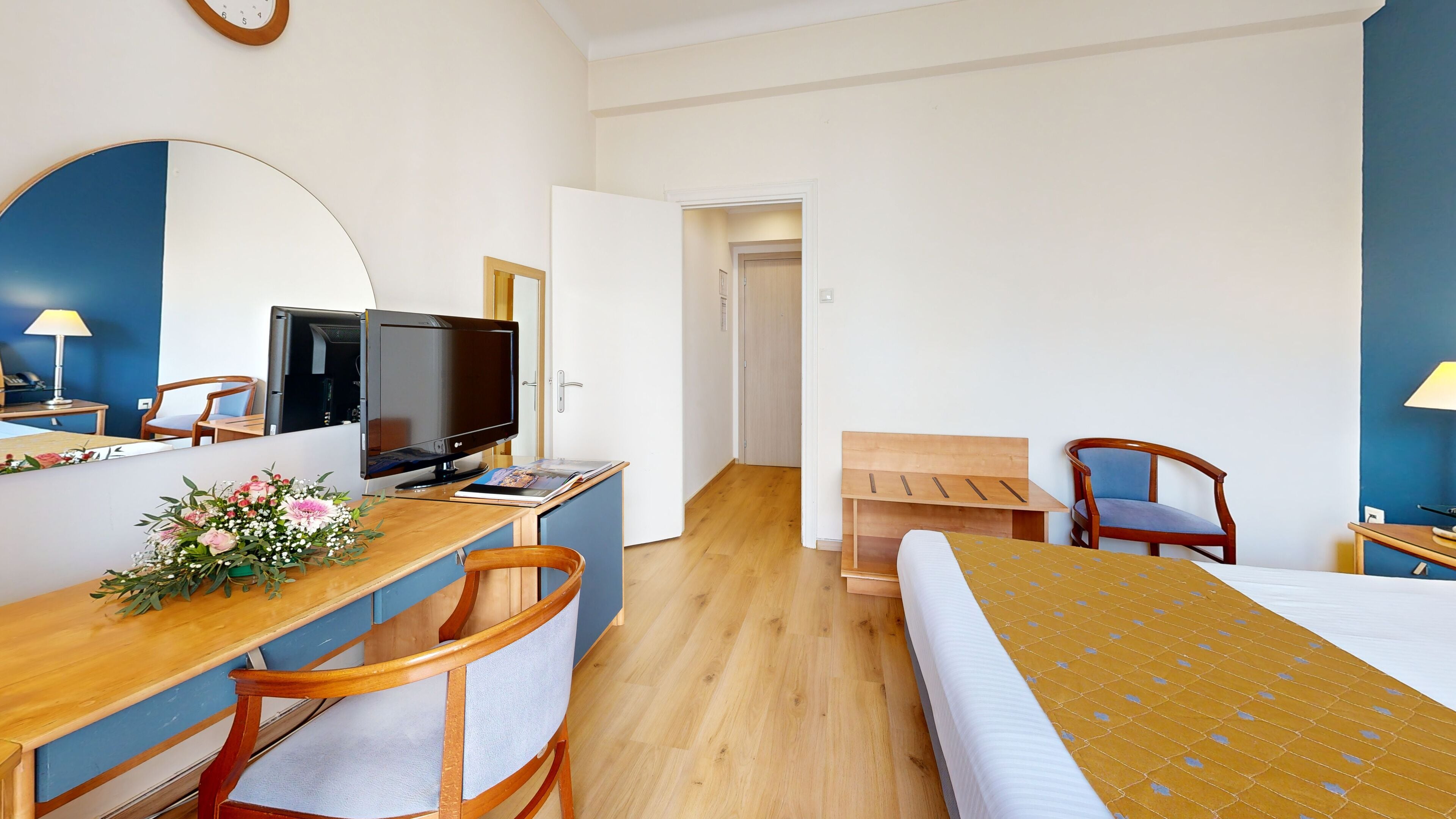 A hotel room with a bed, a desk with a computer, a chair, a TV, and a mirror.