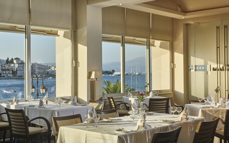 A dining area with tables set for service, large windows offering a view of the sea and buildings, and a modern interior design.