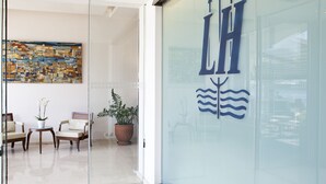 A modern interior with a glass wall displaying a logo, a seating area with chairs and a table, and a large abstract painting on the wall. - Lucy Hotel (Chalcis)
