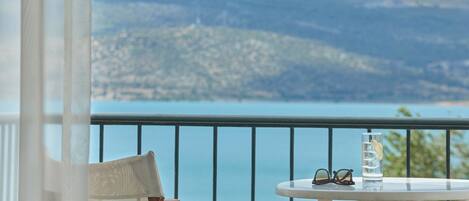 A balcony with a table, a chair, a glass of water, and a pair of sunglasses.