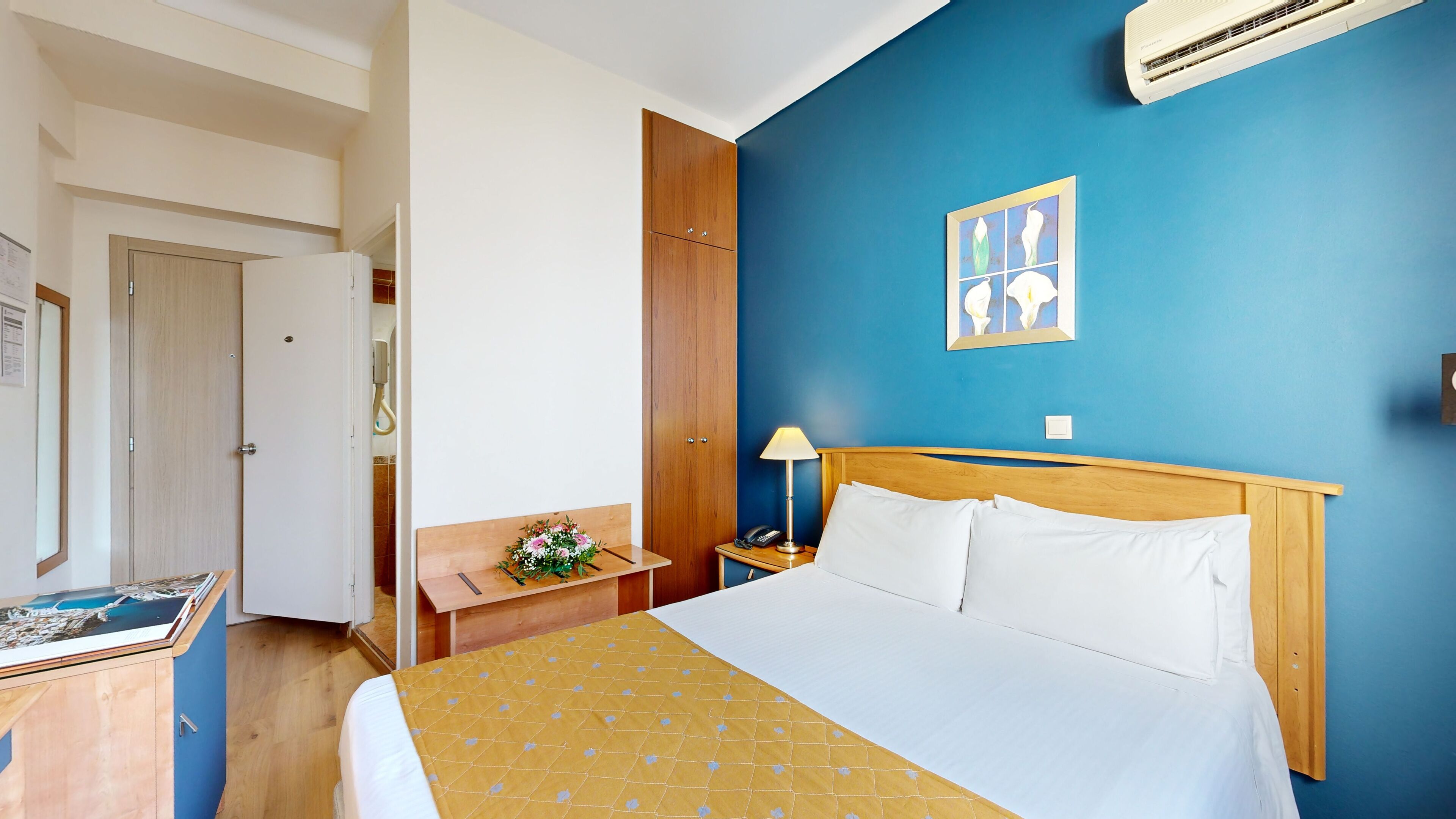 Habitación de hotel con cama, mesita de noche, escritorio, silla, aire acondicionado de pared y puerta.