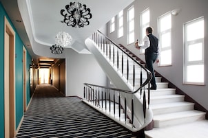 Un vestíbulo de hotel con una escalera, una alfombra estampada y un candelabro.