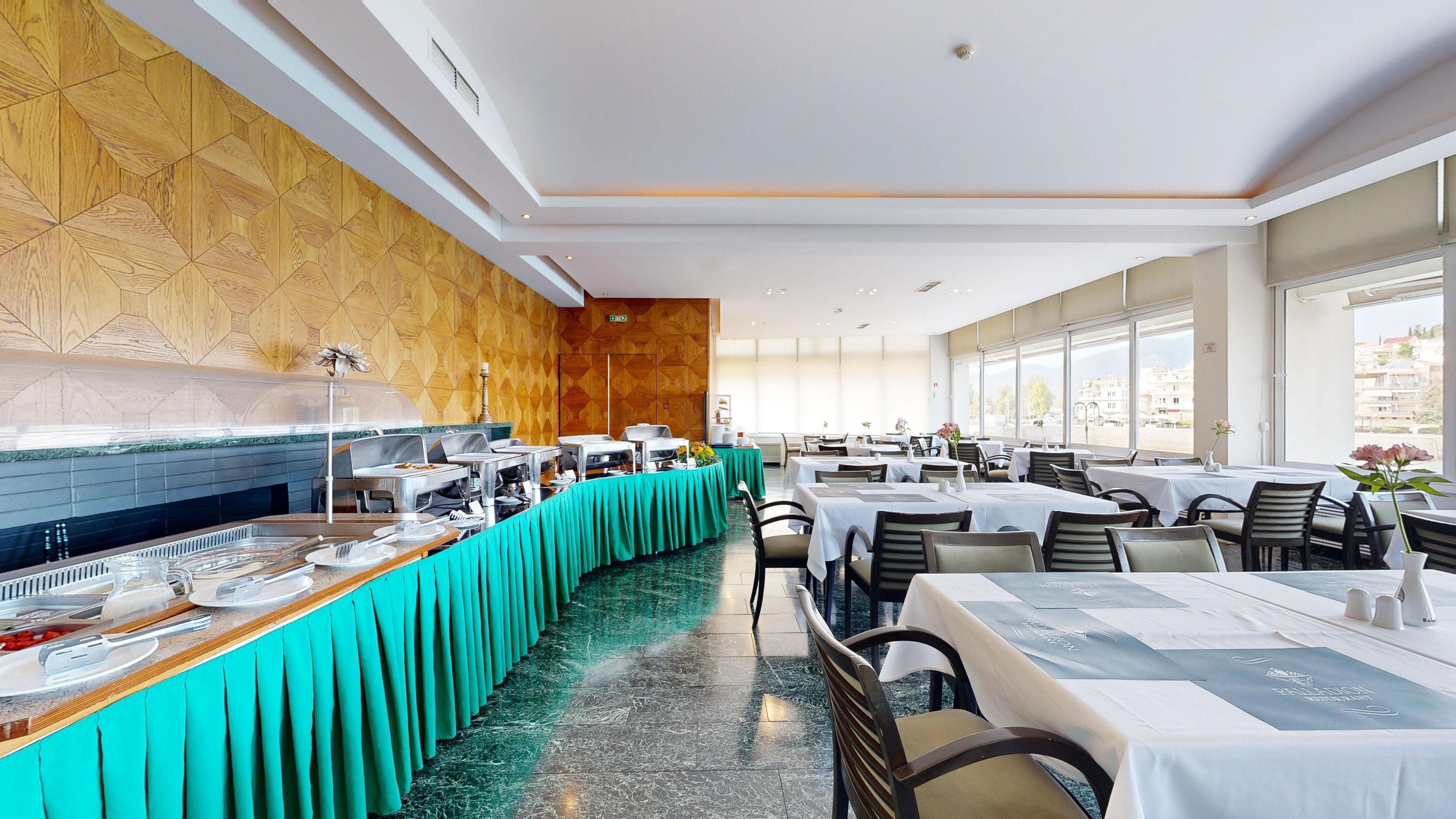 Um restaurante com serviço de buffet, um balcão longo com comida e bebidas, e mesas com cadeiras.