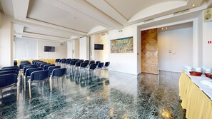A conference room with rows of chairs, a large table, a television, and a painting on the wall. - Lucy Hotel (Chalcis)