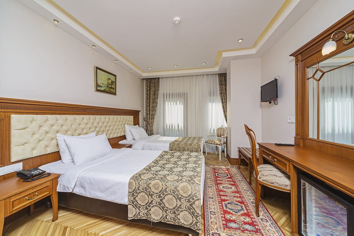 A hotel room with two beds, a wooden desk, a chair, a television, and a large mirror.