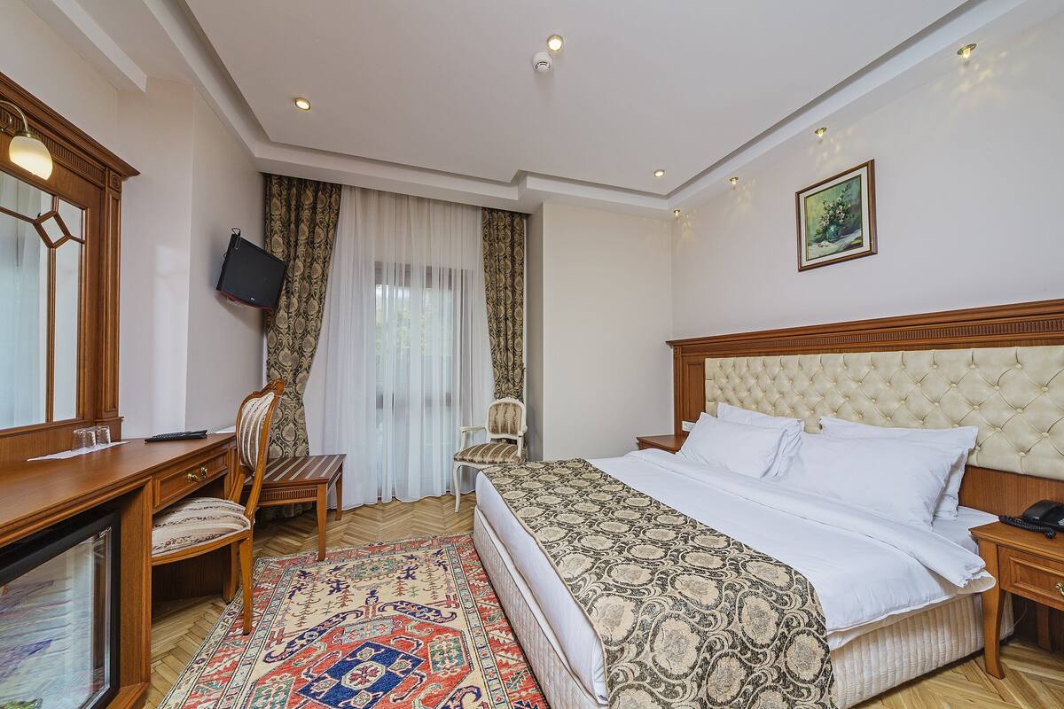 A hotel room with a large bed, a desk with a chair, a television, and a wooden headboard.