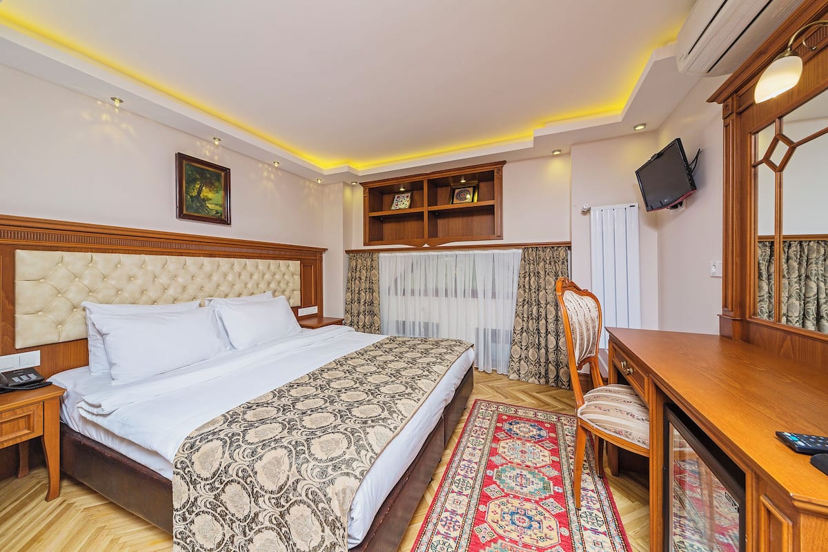 A hotel room with a large bed, a wooden desk, a television, and a bookshelf.