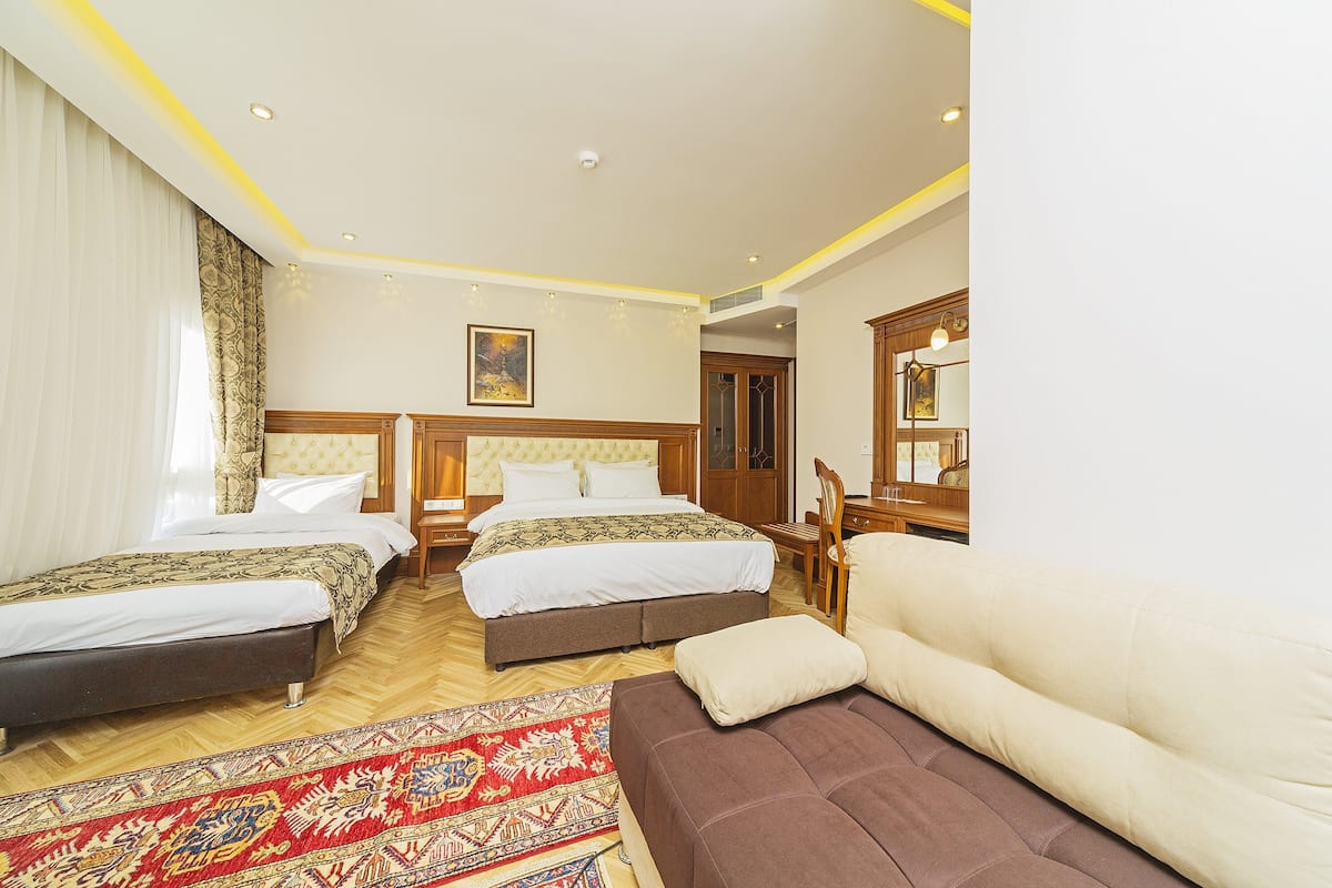 A hotel room with two beds, a sofa, a wooden chair, and a large mirror.