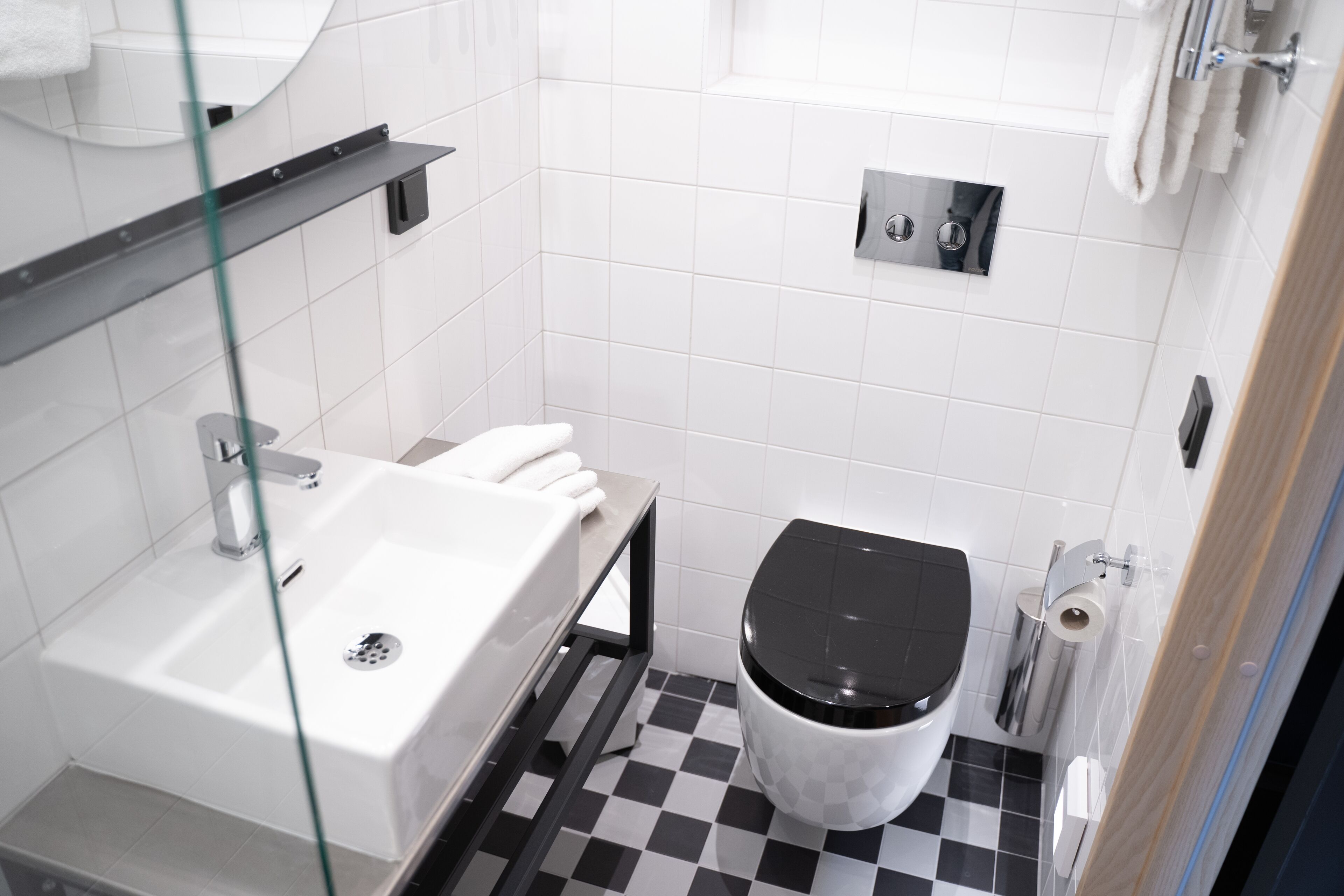 A modern bathroom with a white sink, black toilet, and checkered floor tiles.