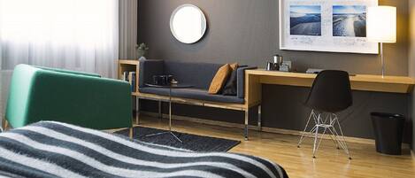 A hotel room with a bed, a desk, a chair, a round mirror, and a framed picture on the wall.