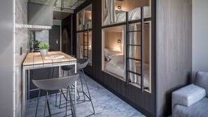 Habitación de hotel pequeña con una cama litera, una kitchenette, una zona de comedor con mesa y sillas, y un ventanal grande con cortinas.
