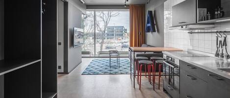 A modern kitchen with a dining area, large windows, and a view of the street.