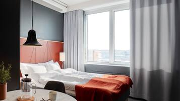 Una camera d'albergo con un letto, una macchina del caffè, un tavolino con una tazza e dei bicchieri, e una finestra con tende.