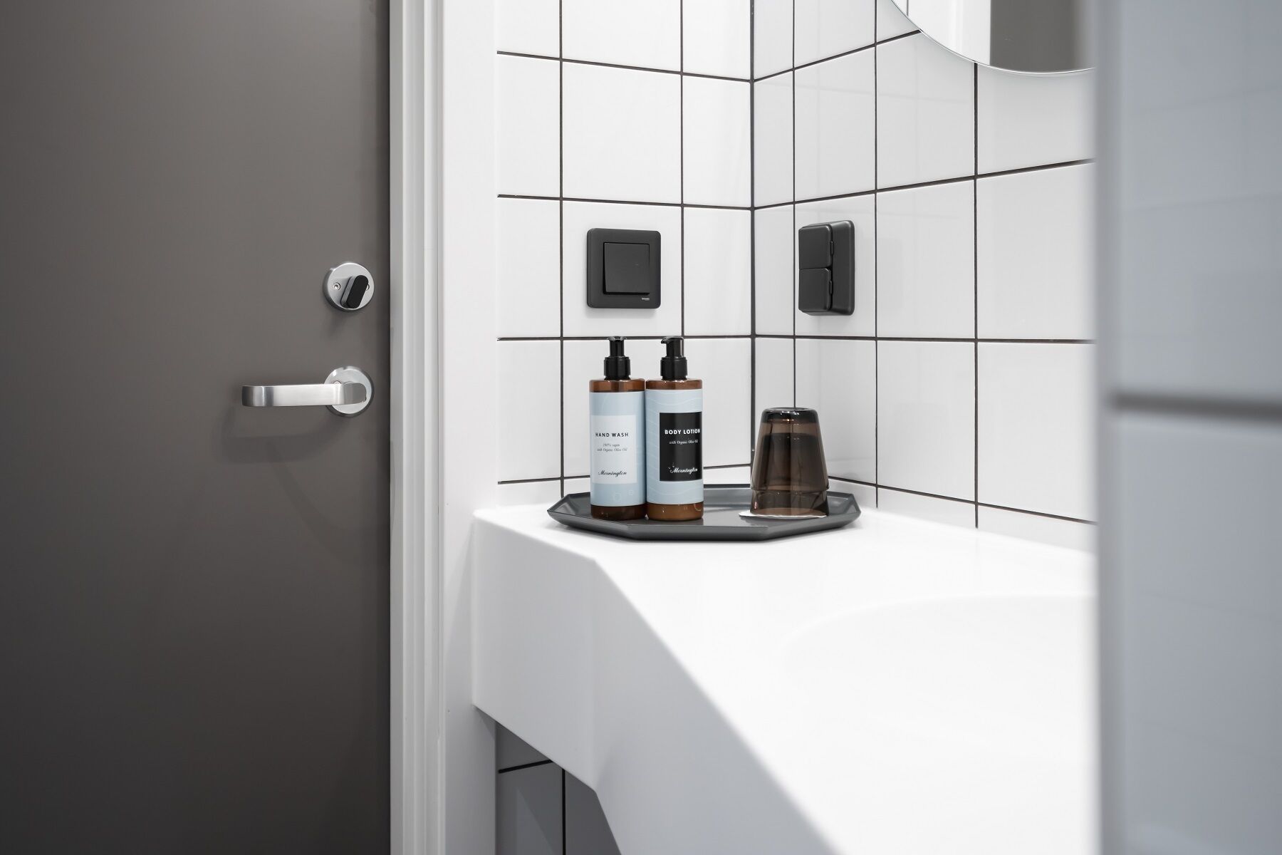 A bathroom with a white sink, two hand wash bottles, a body lotion bottle, and a glass.