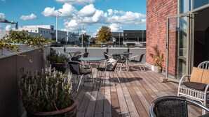 Un patio al aire libre con piso de madera, sillas de metal y plantas en macetas.