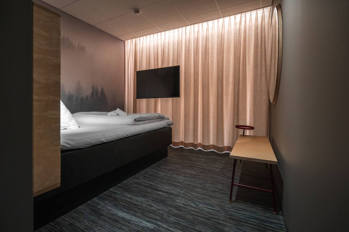 Een moderne hotelkamer met een bed, een flatscreen televisie aan de muur, een klein tafeltje en een vloerbedekking.