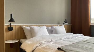 A hotel room with a bed, two bedside tables, a wall-mounted lamp, and a window with curtains.