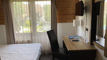 A hotel room with a bed, a desk with a chair, a lamp, and a window with curtains.