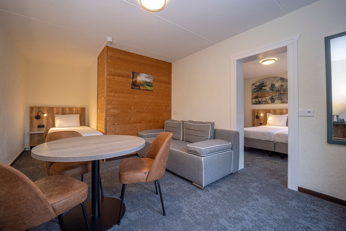 A hotel room with a round table, two sofas, a bed, and a painting on the wall.