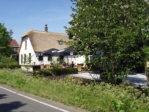 A white building with a thatched roof, outdoor seating, and a garden area.