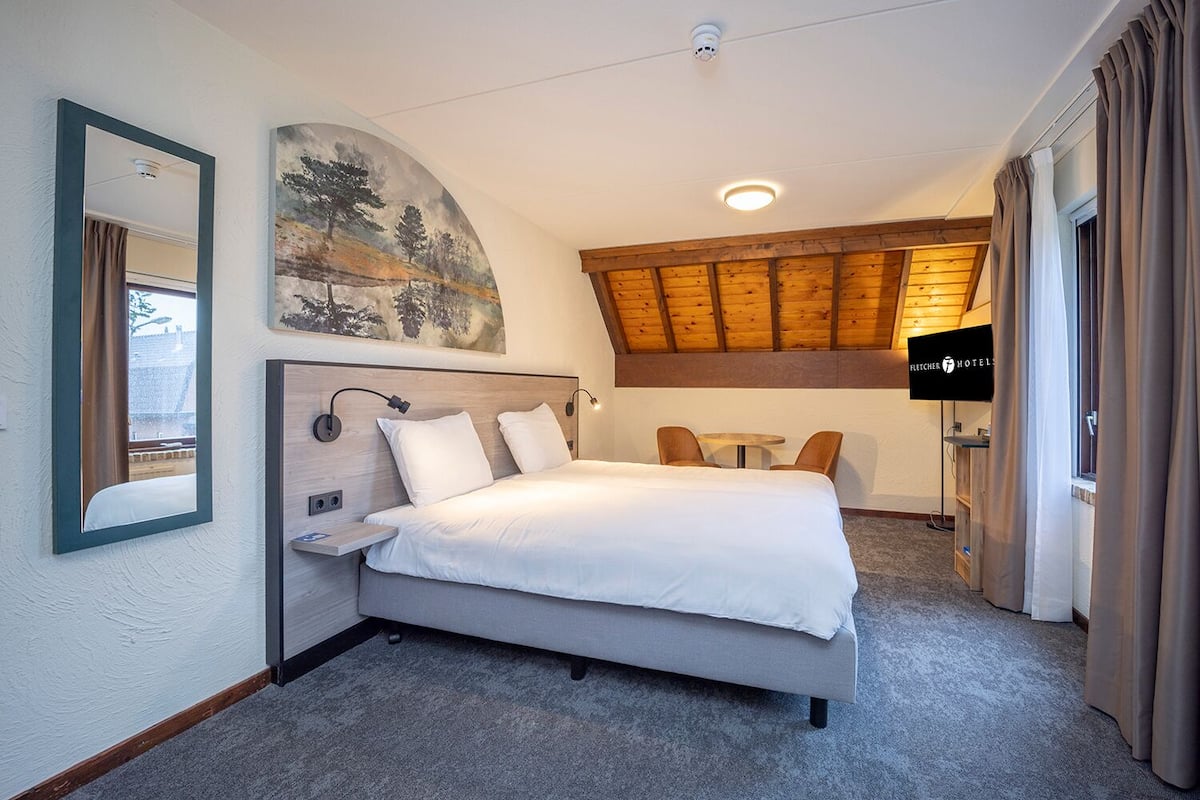 A hotel room with a bed, a TV, a small table, and a painting on the wall.