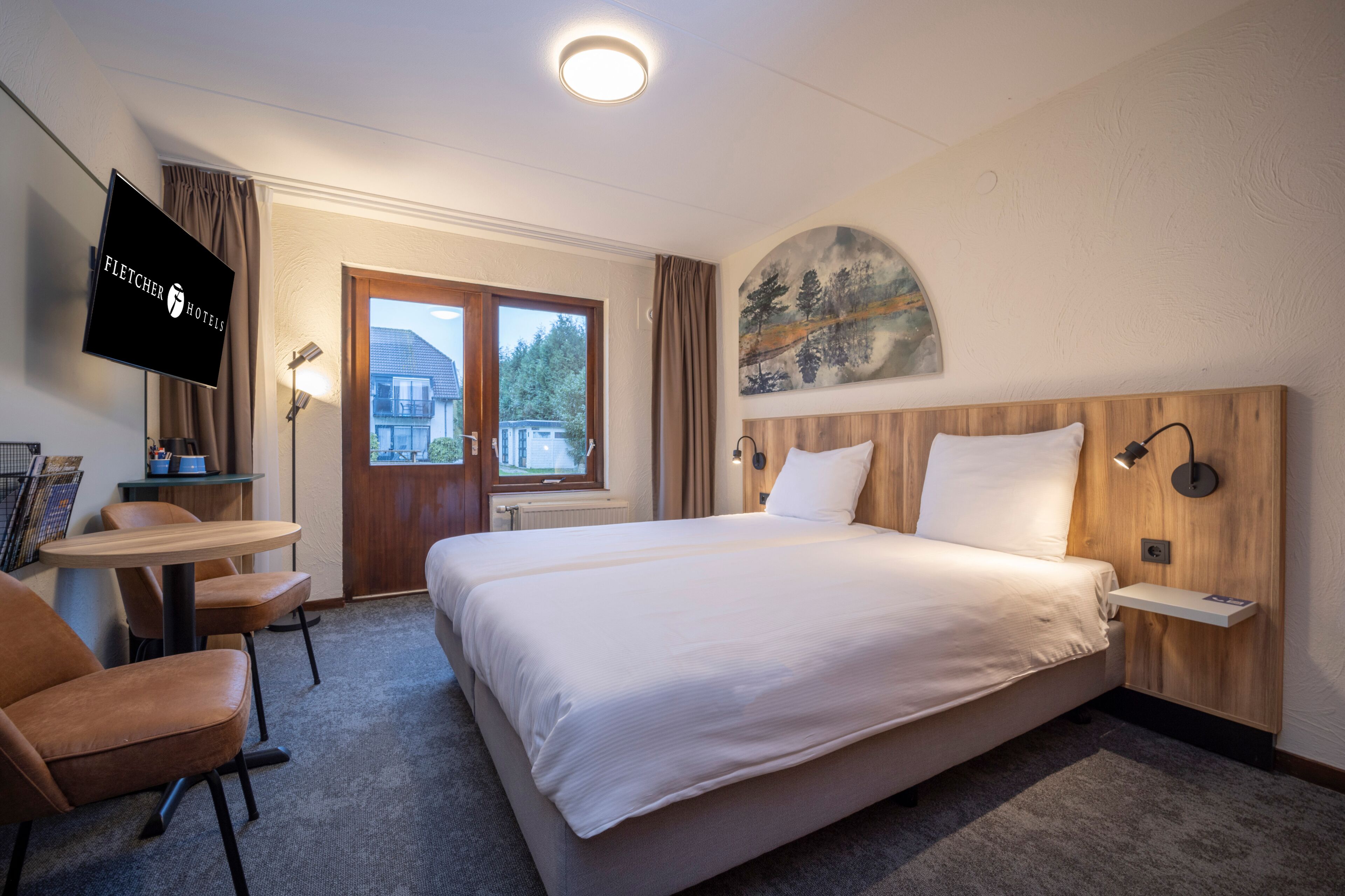 A hotel room with a bed, a desk, a chair, a TV, and a painting on the wall.
