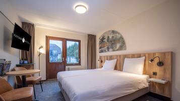 A hotel room with a bed, a desk, a chair, a TV, and a painting on the wall.