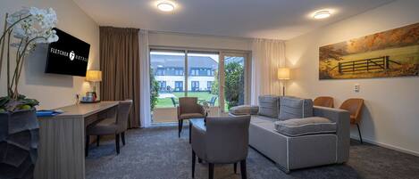 A hotel room with a desk, two chairs, a sofa, a TV, and a painting.