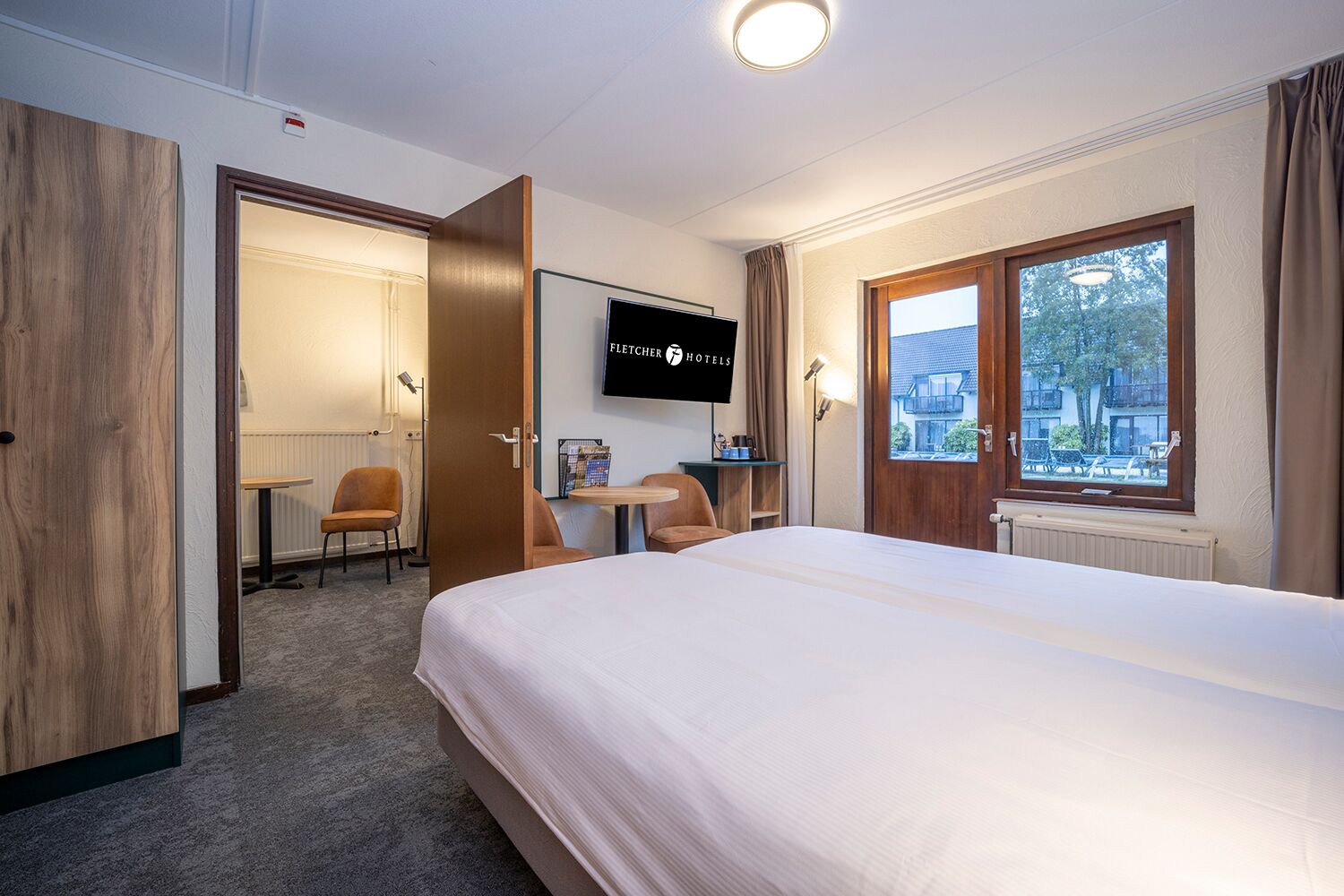 Una camera d'albergo con un letto, una scrivania, una sedia, una televisione e una finestra vista.