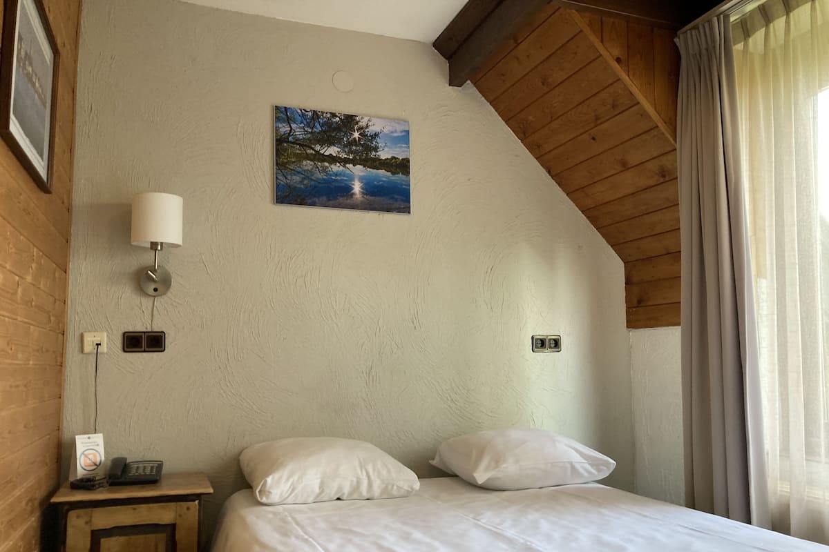 A bedroom with a wooden ceiling, a bed with white bedding, a nightstand with a lamp, and a painting on the wall.