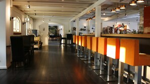 A bar area with a long counter, wooden chairs, and pendant lighting. - Fletcher Hotel De Witte Brug (Lekkerkerk)