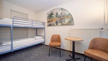 A bunk room with two beds, a round table, two chairs, and a painting on the wall.
