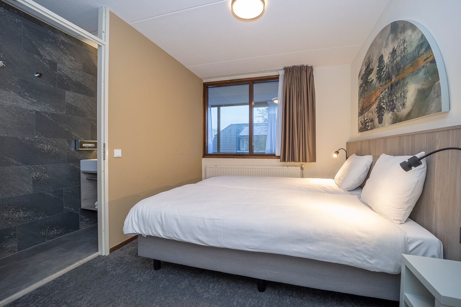 Un dormitorio con cama, ventana, un cuadro y zona de ducha.