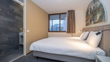 Un dormitorio con cama, ventana, un cuadro y zona de ducha.