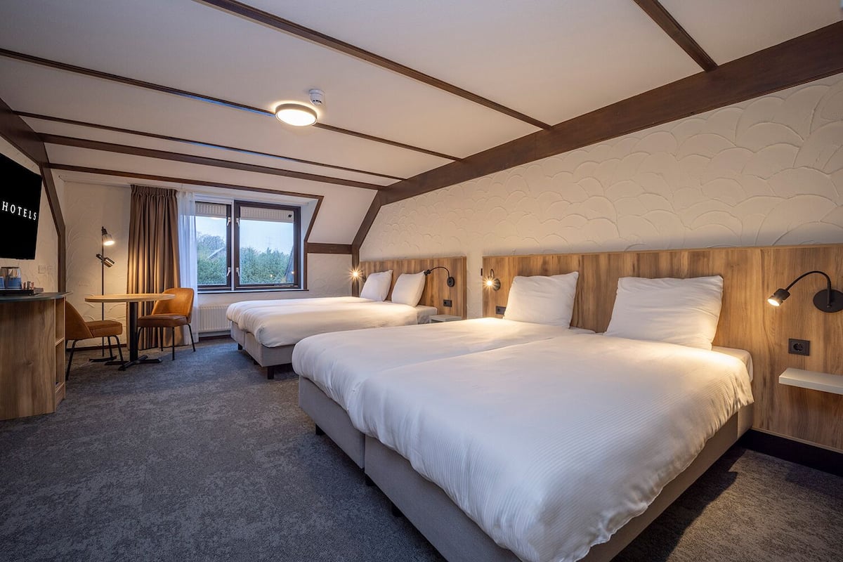 A hotel room with two beds, a desk, a chair, a TV, and a window with curtains.