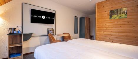 Habitación de hotel con cama, escritorio con tetera, silla, estantería y un cuadro en la pared.