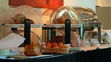 Buffet com diversos alimentos sob cúpulas de vidro, incluindo pães e doces.