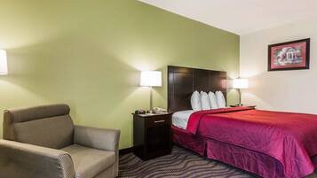 A hotel room with a bed, a chair, a nightstand, and a lamp.