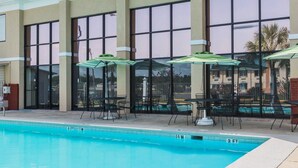 Ein Pool mit Liegestühlen und Sonnenschirmen, große Fenster und eine Gebäudefassade.